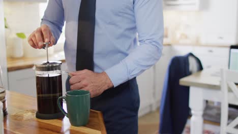 midsection of caucasian man wearing tie, standing in kitchen and making coffee