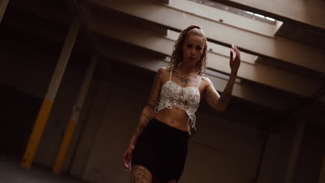 tattooed woman posing confidently in empty industrial hall, gimbal fpv and slow motion