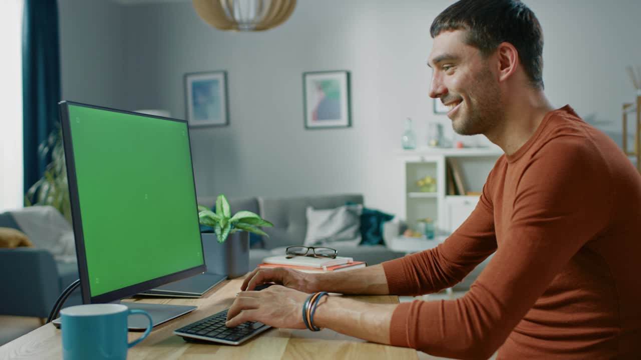 un hombre guapo sentado en su escritorio en casa usa una computadora personal con una pantalla clave de croma.