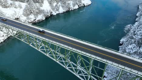 close up aerial view of a car driving on a bridge high up above the water with snow everywhere