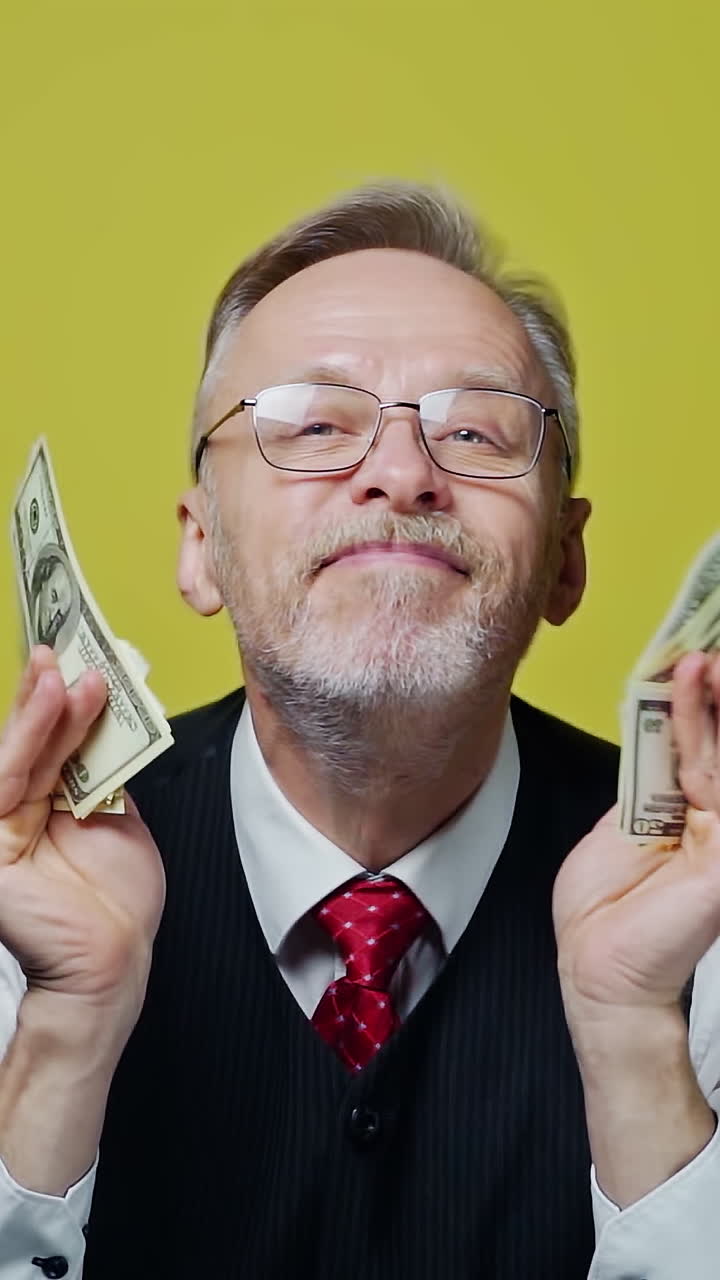 Happy senior man enjoys money. Portrait of an old businessman with many dollar banknotes in his hands. Great business deal. Vertical video