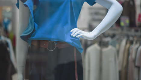 close-up of mannequin wearing stylish blue top paired with brown belt and black trousers, hand posed on hip in retail store window display