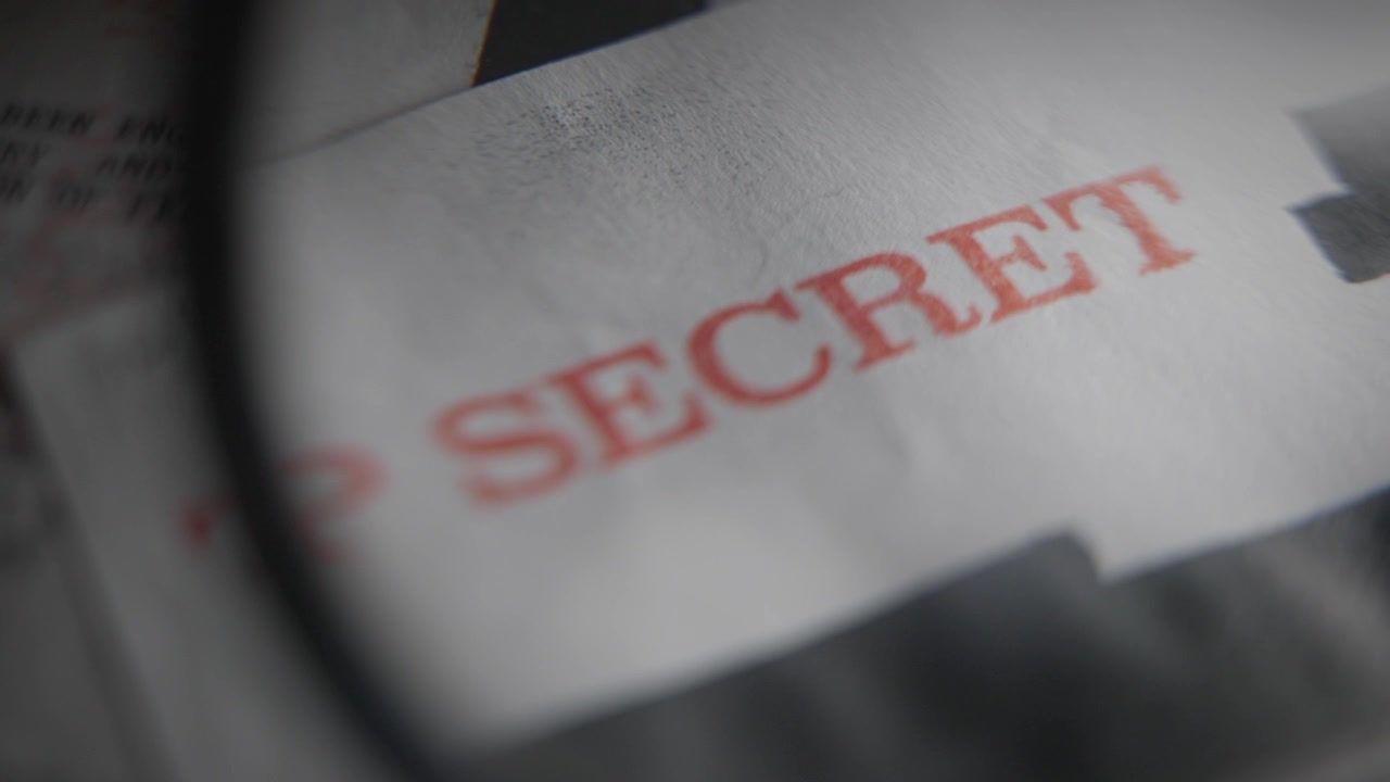 Lente d'ingrandimento puntata su un timbro rosso di autorizzazione di sicurezza Top Secret su un rapporto di intelligence classificato o un fascicolo di documenti governativi militari. Documenti trapelati da un informatore o informazioni riservate esposte.