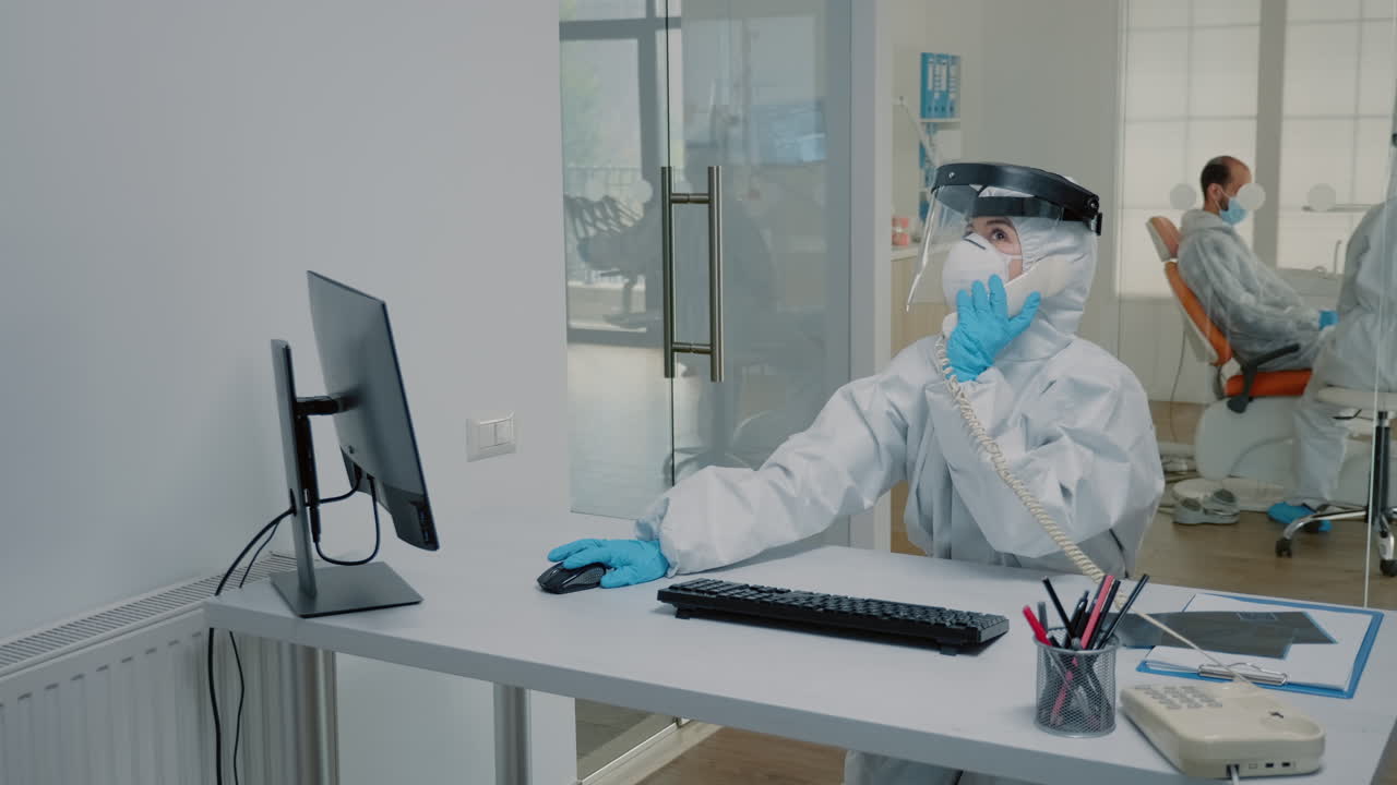 Dentistry nurse in protection suit sitting at desk
