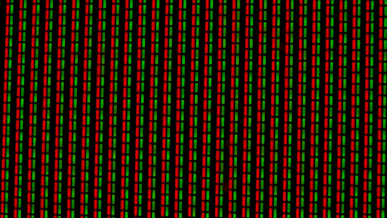 Working pixels in the screen color TV, with a video playback close up. Green and red pixels flicker against a black background. Macro