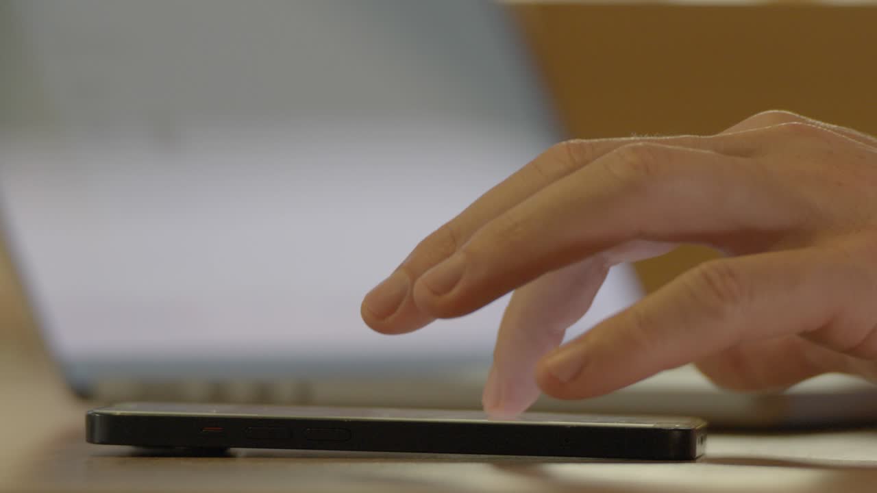 disparo en cámara lenta de una mano usando un teléfono inteligente y luego cambiando a escribir en una computadora