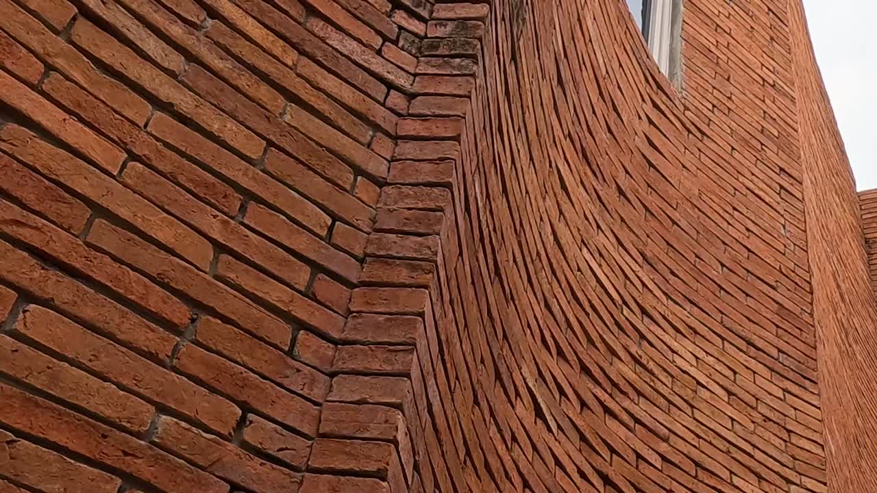 Close-up view of a curved brick wall showcasing intricate masonry and a small window.