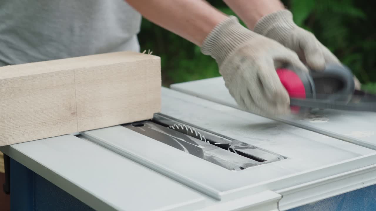 Gloved hand places solid wood block across table saw outdoors putting on ear protection