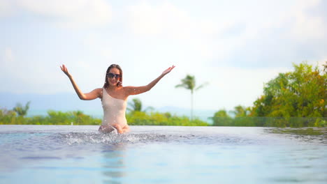 Eine-Attraktive-Frau,-Die-Am-Rand-Eines-Schwimmbeckens-Sitzt,-Spritzt-Spielerisch-Wasser-In-Die-Luft