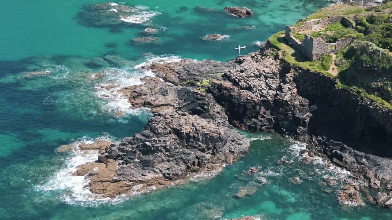 Angled aerial circle left around ruins near the water along the Cornwall coastline on a sunny day