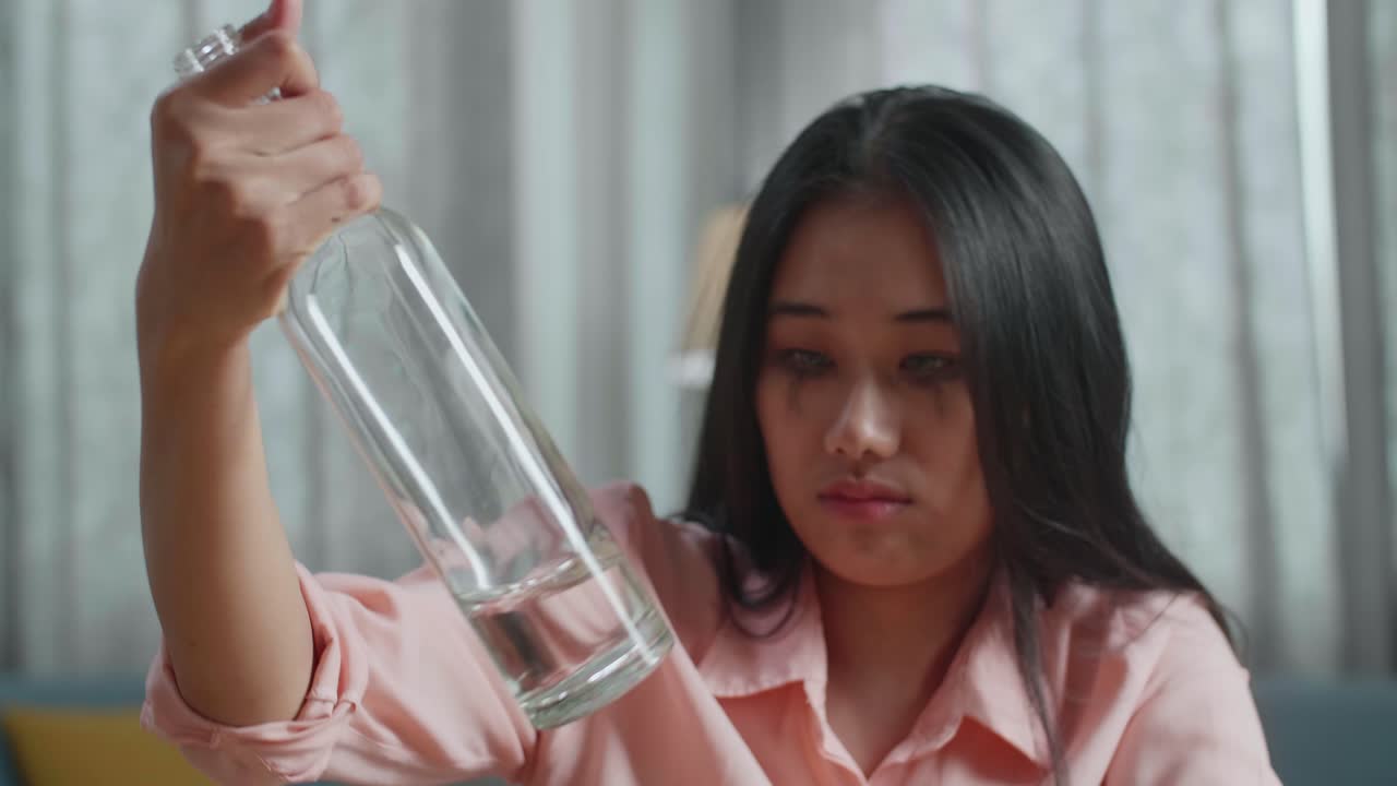 술에 취한 우울한 아시아 여성이 집에서 병에서 보드카를 마시고 있는 장면