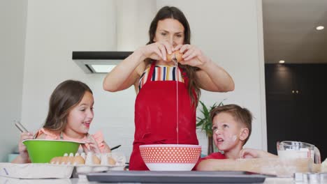 madre, hija e hijo caucásicos felices rompiendo huevos, horneando juntos en la cocina