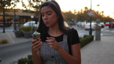 A-cute-young-hispanic-woman-eating-a-messy,-dripping-ice-cream-cone-walking-on-a-city-street