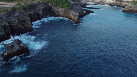 nusa ceningan's blue lagoon and coastal cliffs with ocean waves in indonesia from an aerial drone tilt down