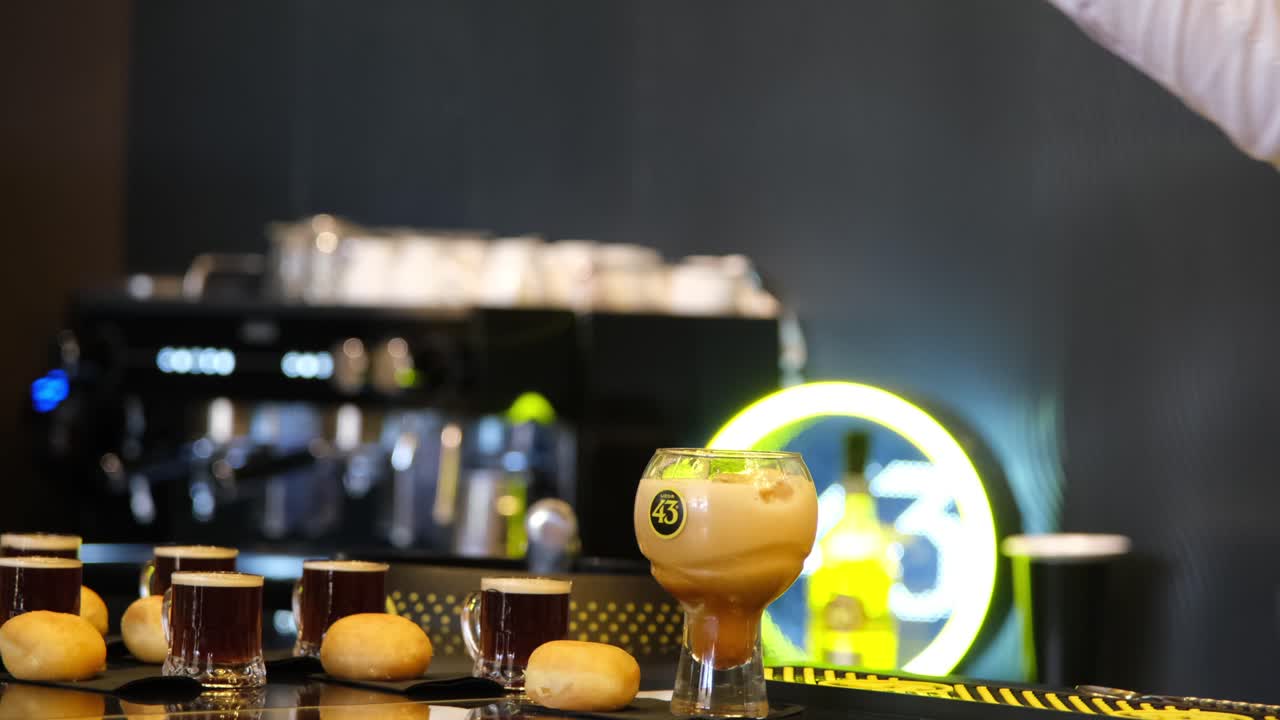A person carefully pours a coffee mix infused with Licor 43 into a glass adorned with the iconic “43” logo, crafting a delicious, aromatic drink.
