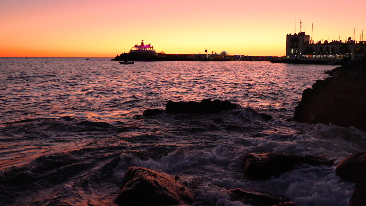 Sea waves hitting the reef and rocks and water jumps on stones during sunset orange color looking out at the edge of Grand Canary Island 4k slow motion capture at 60fps.