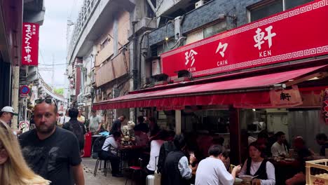 busy street scene with people dining at an outdoor restaurant under red signage in an urban setting