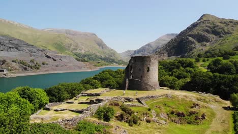 aerial shot of castle ruins in wales with the beautiful countryside in the background including a lake, rolling hills, and trees