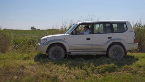 Cowboy-driving-his-4x4-jeep-through-the-the-rural-grass-in-a-farm-field