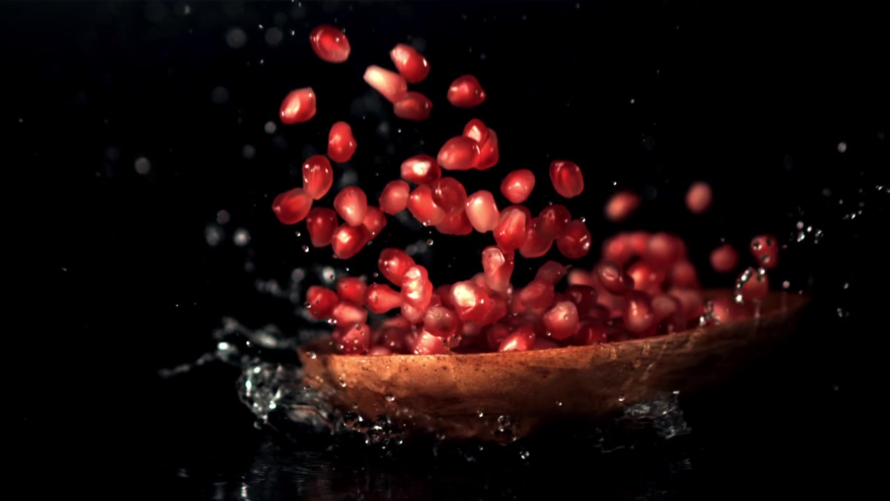 Røde granatæblekerner, der sprøjter med vand i slowmotion