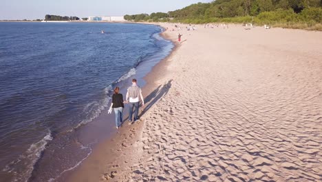 Toma-Aérea-De-Una-Pareja-Joven-Caminando-En-La-Playa,-Abrazándose,-Tomándose-De-La-Mano