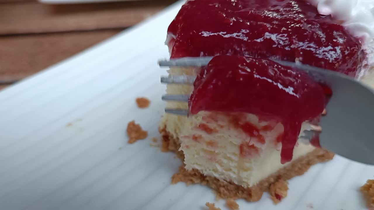 A fork slicing a piece of cheesecake with berry jam