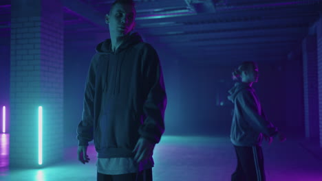 two hip-hop dancers in neon light dance together in blue and purple colors. women enjoying hip hop moves in dark studio with smoke and lighting.