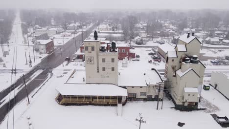 Old-grain-elevator-facility-and-small-township-during-snowfall,-aerial-drone-view