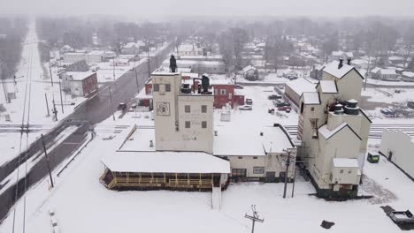 Antigua-Instalación-De-Elevador-De-Granos-Y-Pequeño-Municipio-Durante-Las-Nevadas,-Vista-Aérea-De-Drones