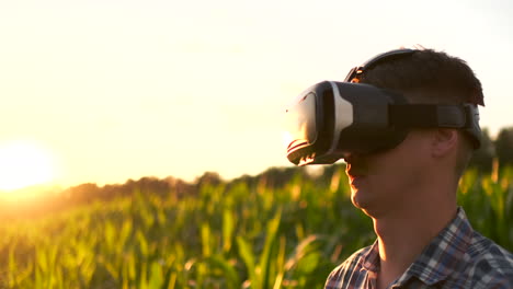 A-modern-farmer-in-a-VR-helmet-drives-a-corn-crop-standing-in-a-field-at-sunset-in-the-sun.-The-concept-of-smart-fields-of-use-of-neural-networks-in-agriculture.-The-use-of-artificial-intelligence-to-agriculture-and-harvest