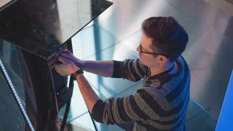 man adjusting cables and connectors on digital display screen in modern video production studio, focused on configuration, wearing striped sweater and id badge, with blue lights and backdrop