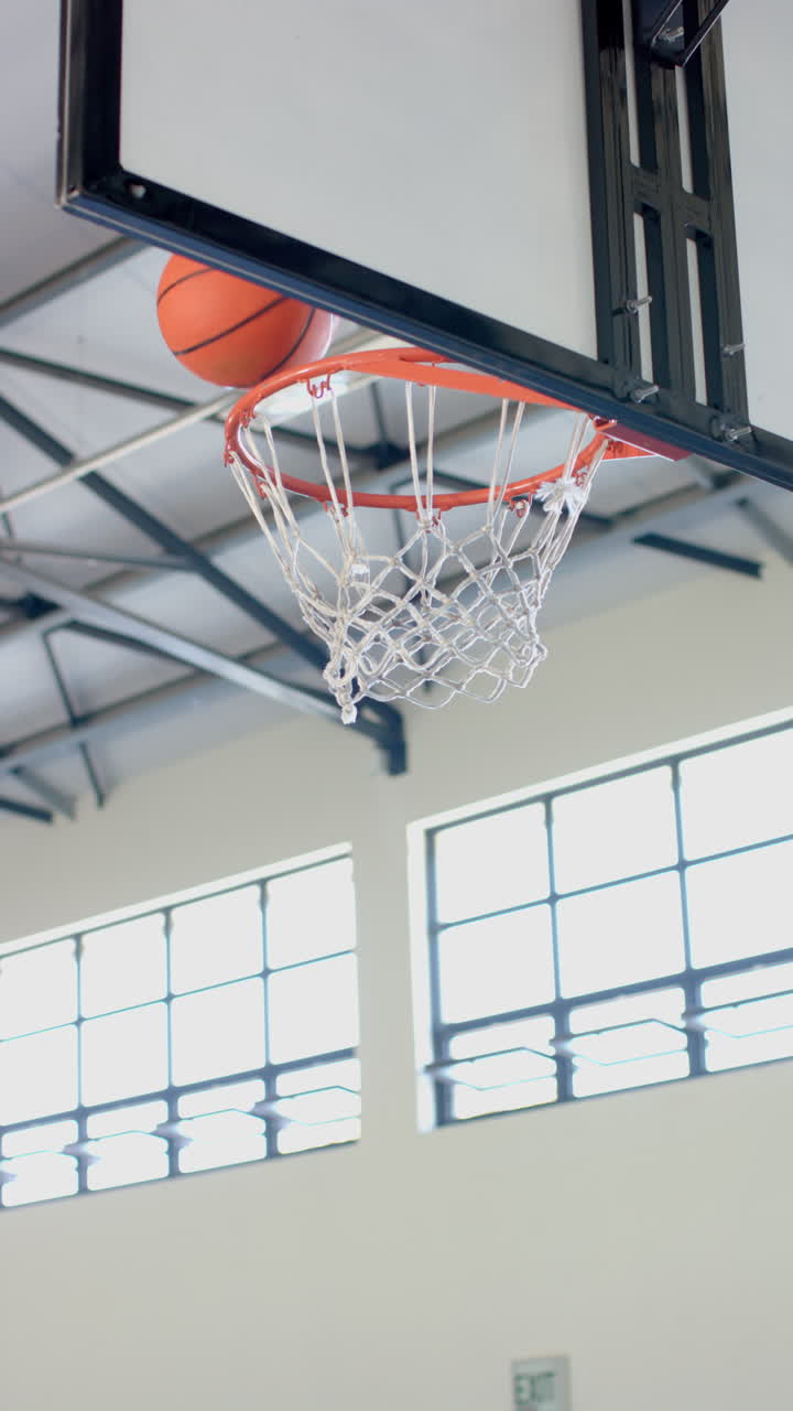 Vertical video: Basketball hoop in indoor gymnasium with net and backboard, ready for game, copy spa