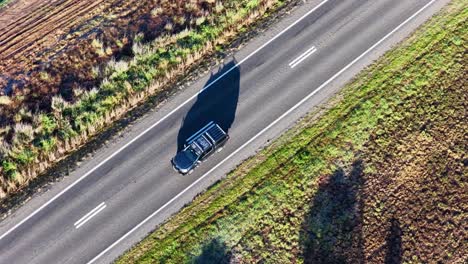a single vehicle travels along a sunlit countryside road in tamworth, nsw, australia, captured from above with steady drone movement and vivid natural lighting