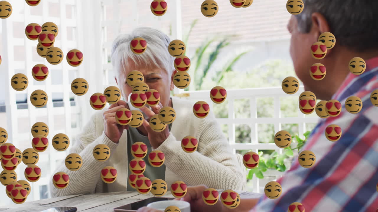 Face emojis floating against african american senior couple drinking coffee together at home