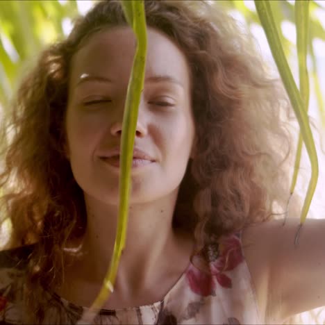 relaxed woman standing behind palm leaves