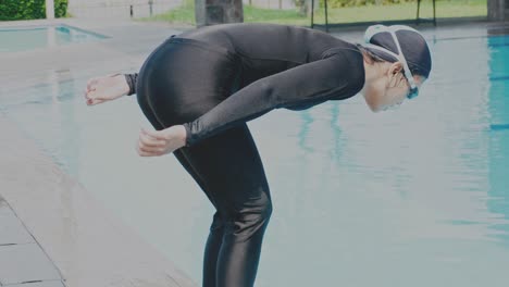 young woman wear black swimsuit and goggle, stands on a springboard preparing to jump into the water