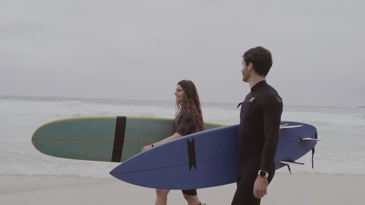due persone che camminano sulla spiaggia con tavole da surf