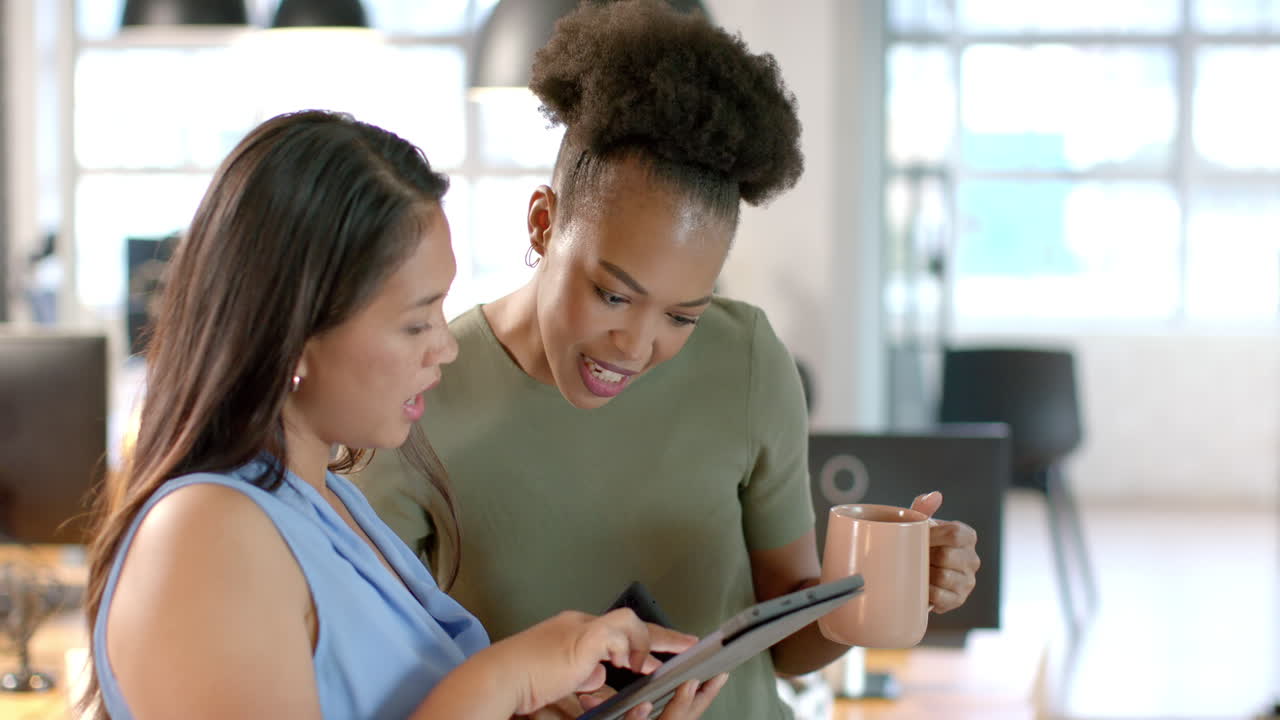 Young African American woman shares a tablet screen with a biracial woman in a business office