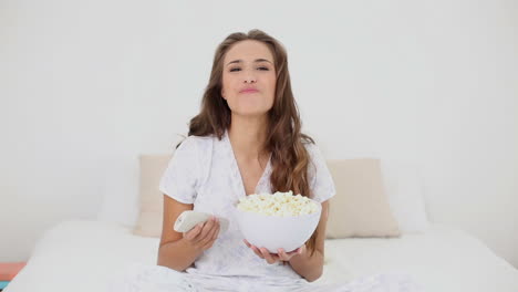 mujer joven comiendo un plato de palomitas de maíz en la cama y viendo la televisión