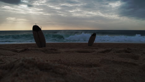 Silhouette-of-a-man-in-a-wetsuit-running-out-of-the-sea,-taking-a-surfboard-stuck-in-the-sand-and-going-surfing