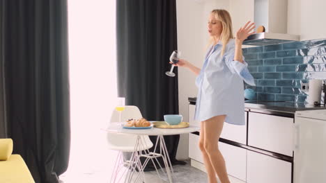 blonde woman with glass of red wine dancing at home.