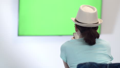 girl sits in font of a geen sreen tv and uses phone, green chroma key screen tv, relaxing on a couch