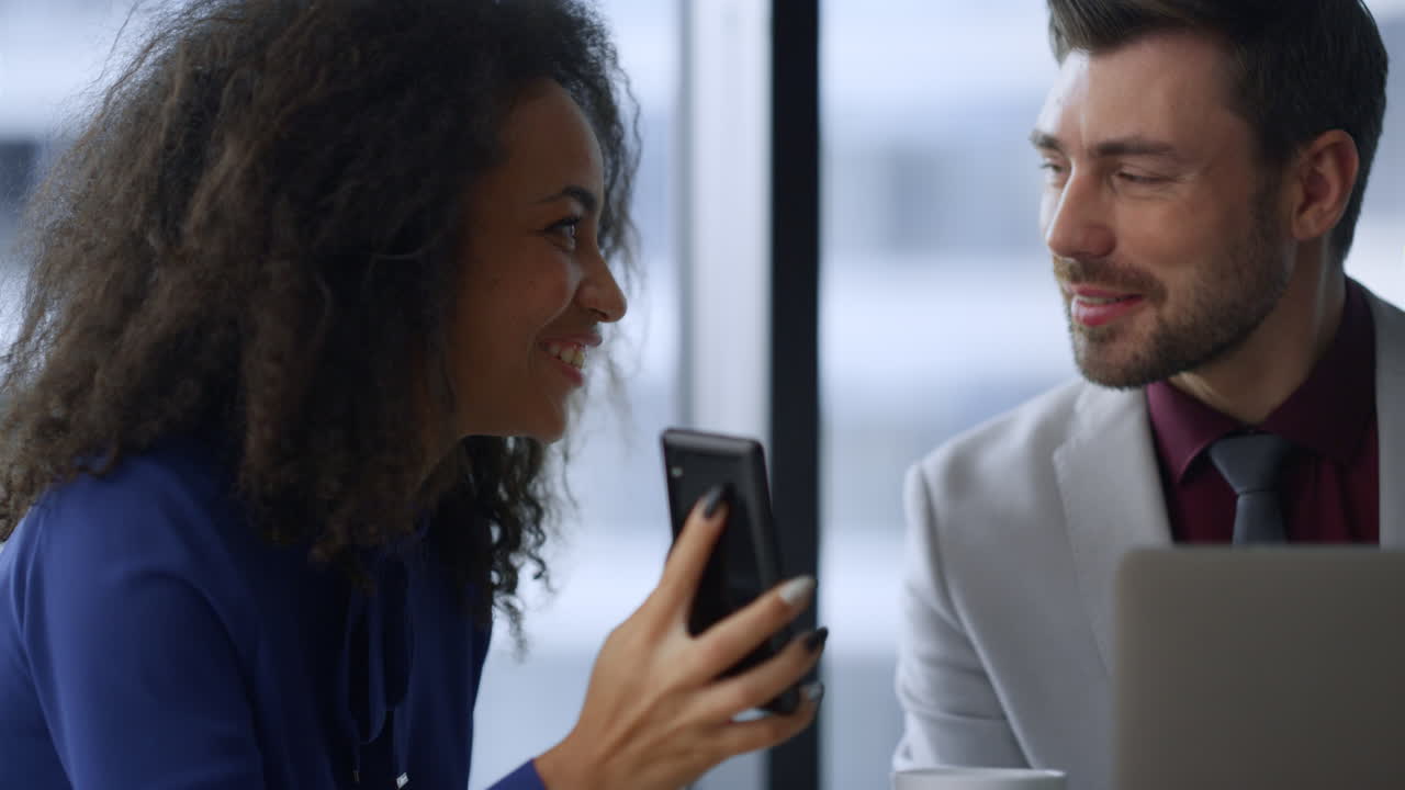 feliz mujer de negocios mostrando teléfono compartiendo buenas noticias con un hombre colega en la oficina