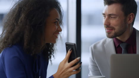 Happy-businesswoman-showing-phone-sharing-good-news-with-man-colleague-in-office