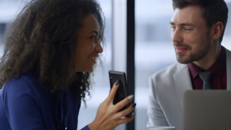 mulher de negócios feliz mostrando telefone compartilhando boas notícias com homem colega no escritório