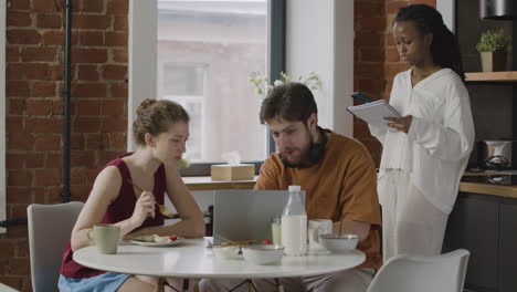 tres compañeros de cuarto desayunando y revisando notas en la computadora y el cuaderno en casa 1