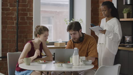 three  roommates having breakfast and reviewing notes on computer and notebook at home 1