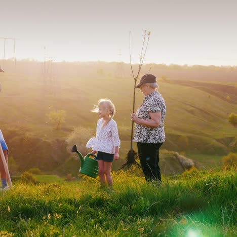 Eine-ältere-Frau-Mit-Zwei-Enkelkindern-Ein-Junge-Und-Ein-Mädchen-Pflanzen-Gemeinsam-Einen-Baum