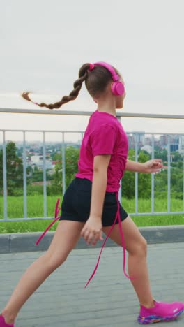 A Young Girl in Vibrant Pink Attire Enjoying an Energetic Dance Routine on a Scenic Outdoor Path, Embracing Joyful Movement with Headphones on