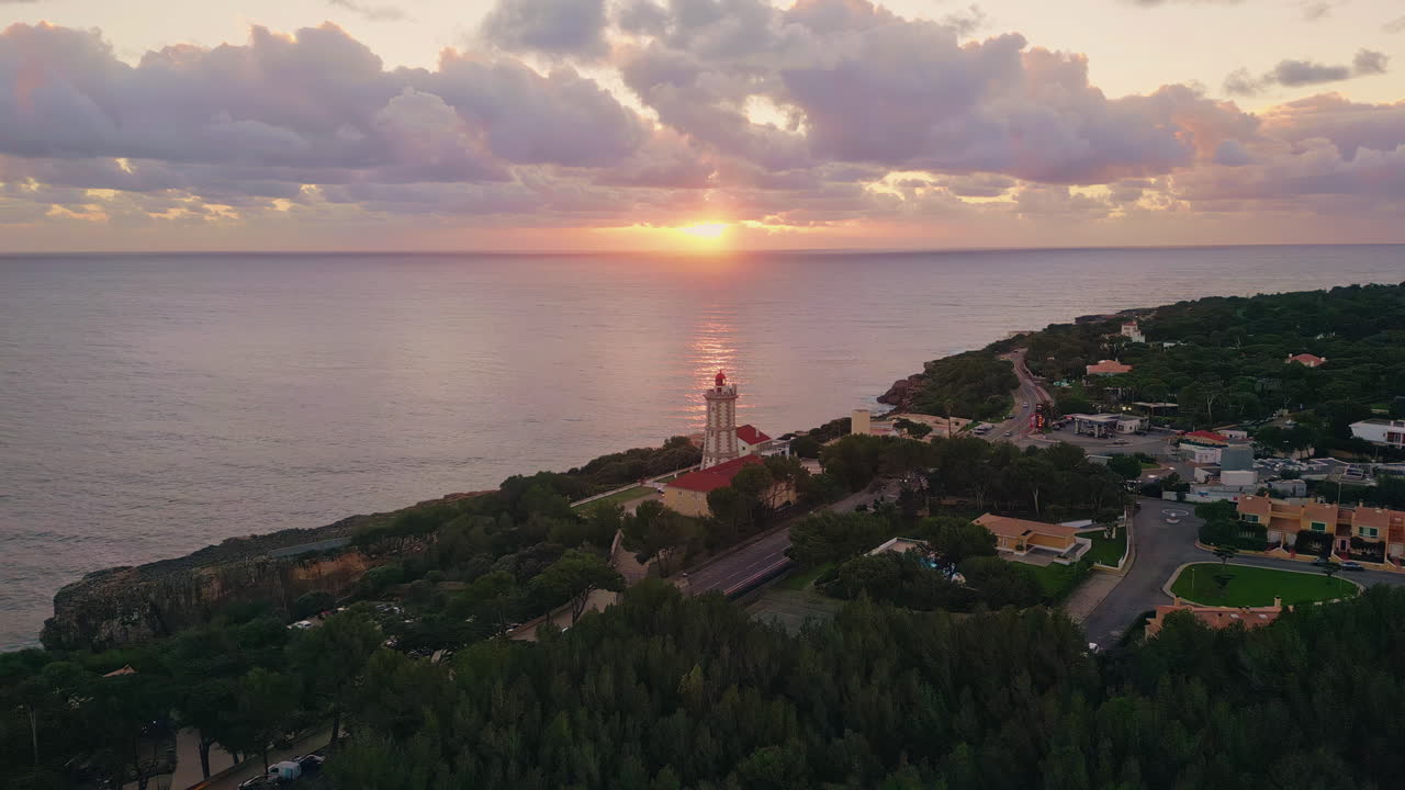 Evening light illuminating lighthouse and coastal town aerial. Scenic sunset